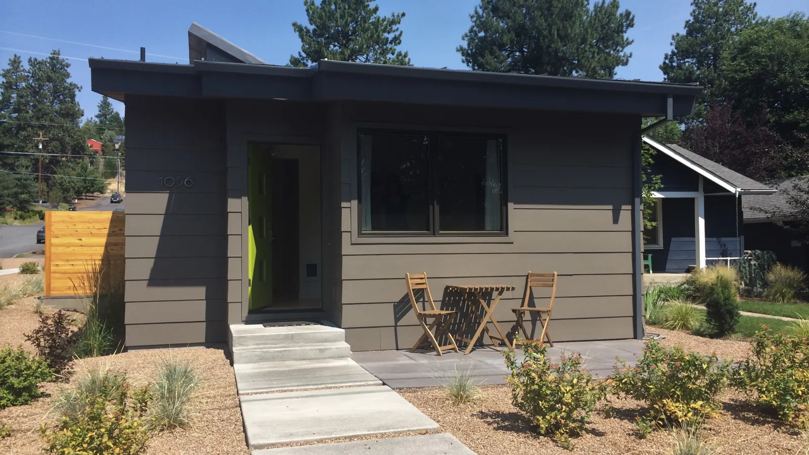 A detached backyard ADU with a flat roof, a bright green front door and a small patio