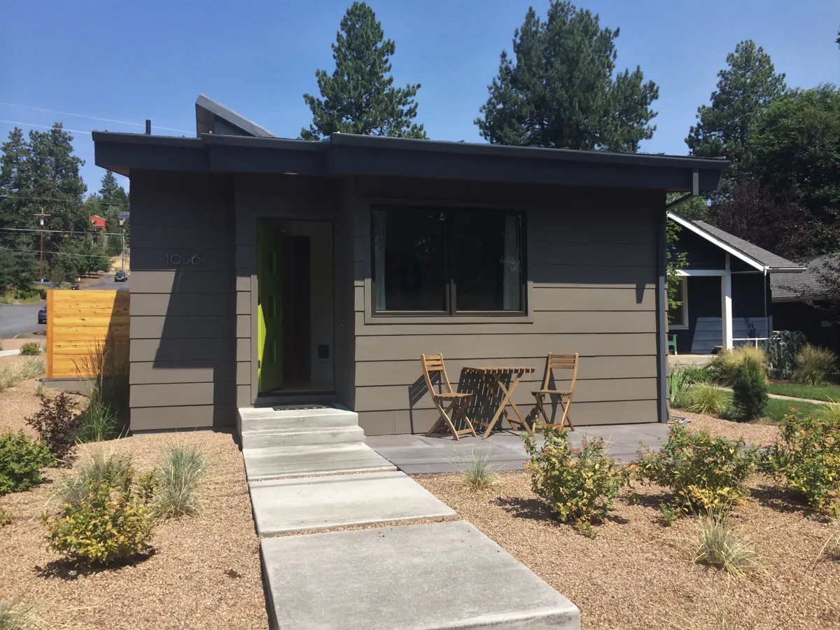 A detached backyard ADU with a flat roof, a bright green front door and a small patio